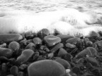Un turbato e malinconico equilibrio, che avvicina gli elementi "Acqua" e "Terra". La scelta del bianco/nero annienta totalmente il calore del sole che batte sull'acqua e sulle pietre, rendendo fresco e intenso il momento del contatto tra i due elementi.